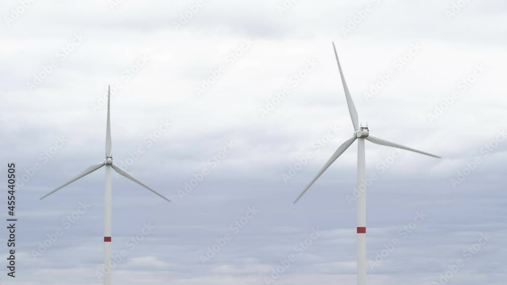 Motion the blades of a large wind turbine in a field against a background of cloudy grey sky on the horizon with a beautiful hills. Alternative energy sources. Windy park. Ecological energy.Industrial Motion the blades of a large wind turbine in a field against a background of cloudy grey sky on the horizon with a beautiful hills. Alternative energy sources. Windy park. Ecological energy.Industrial