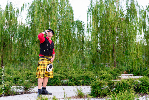 funny and unusual 50-year-old man, dressed as a Scotsman in a kilt and vest, explores a city park and wonders where to find him