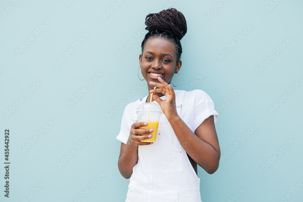 Young cheerful woman drinking a juice against blue wall and looking at camera Young cheerful woman drinking a juice against blue wall and looking at camera