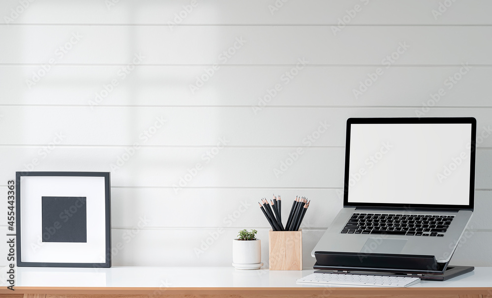 Mockup blank screen laptop on stand and wooden frame on wooden table with white wooden wall. Mockup blank screen laptop on stand and wooden frame on wooden table with white wooden wall.