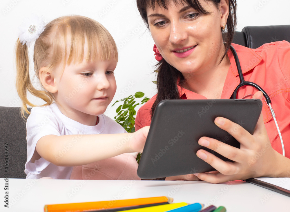A woman doctor, a pediatrician, shows a 3-4 year old girl cartoons on a tablet. An individual approach to the treatment of each child. Pediatric medicine A woman doctor, a pediatrician, shows a 3-4 year old girl cartoons on a tablet. An individual approach to the treatment of each child. Pediatric medicine