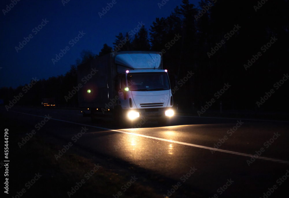 The van transports cargo with the headlights on at night, in the background. Freight industry, international