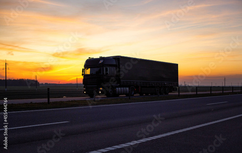 A truck with a tilt semitrailer transports a groupage cargo against the backdrop of an evening sunset, twilight. The concept of the cost of transportation of goods by trucks, industry. Freight
