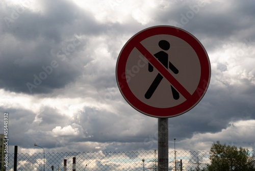 a road forbidding sign "pedestrians are not allowed to walk" against the background of a gray cloudy sky and a metal fence