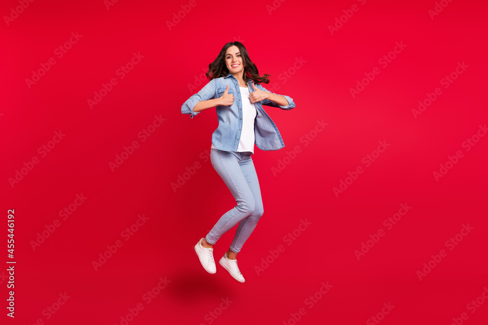 Full length photo of young girl happy positive smile jump up show thumbs-up feedback isolated over red color background