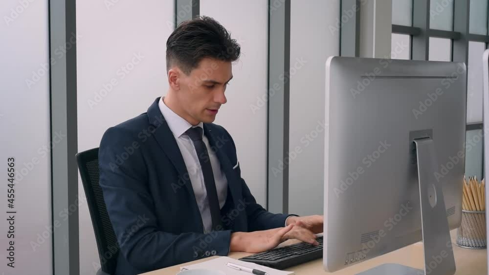 Handsome smart business man in suit outfit working in front of computer with smart and confident typing on keyboard in modern office Handsome smart business man in suit outfit working in front of computer with smart and confident typing on keyboard in modern office