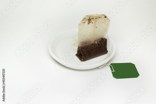 used tea bag with a long thread and paper green lable, on a small white saucer with tea stains