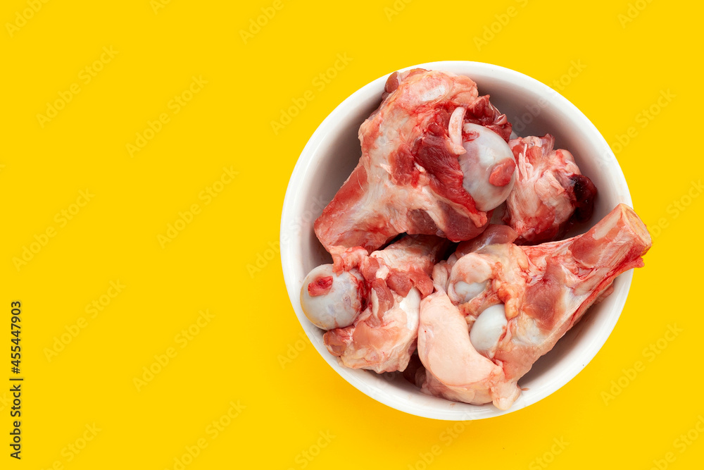 Raw pork bones in white bowl on yellow background.