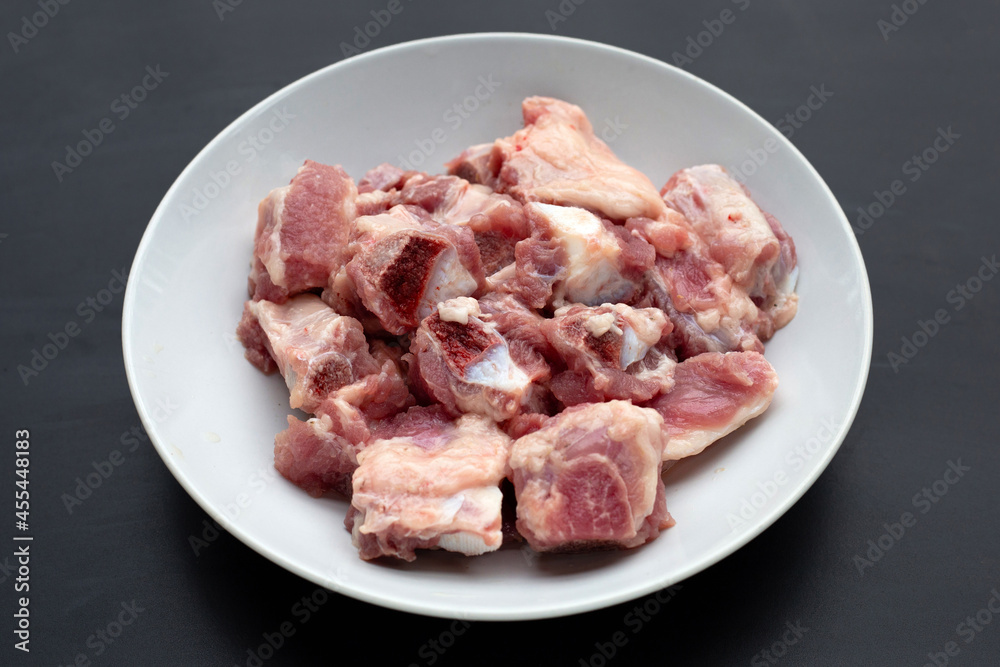 Raw pork ribs in white plate on dark background.