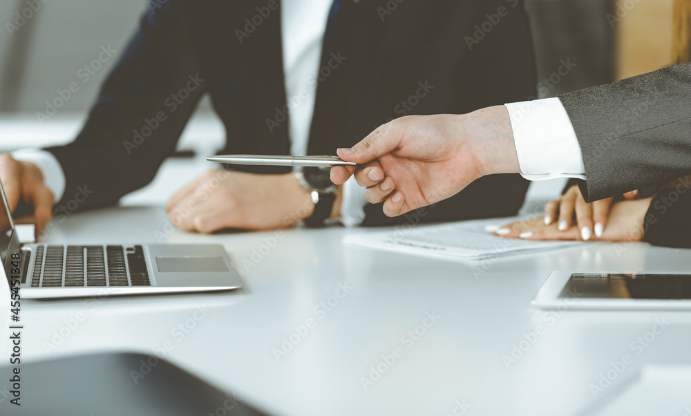 Unknown businessmen and woman sitting, using laptop computer and discussing questions at meeting in modern office, close-up