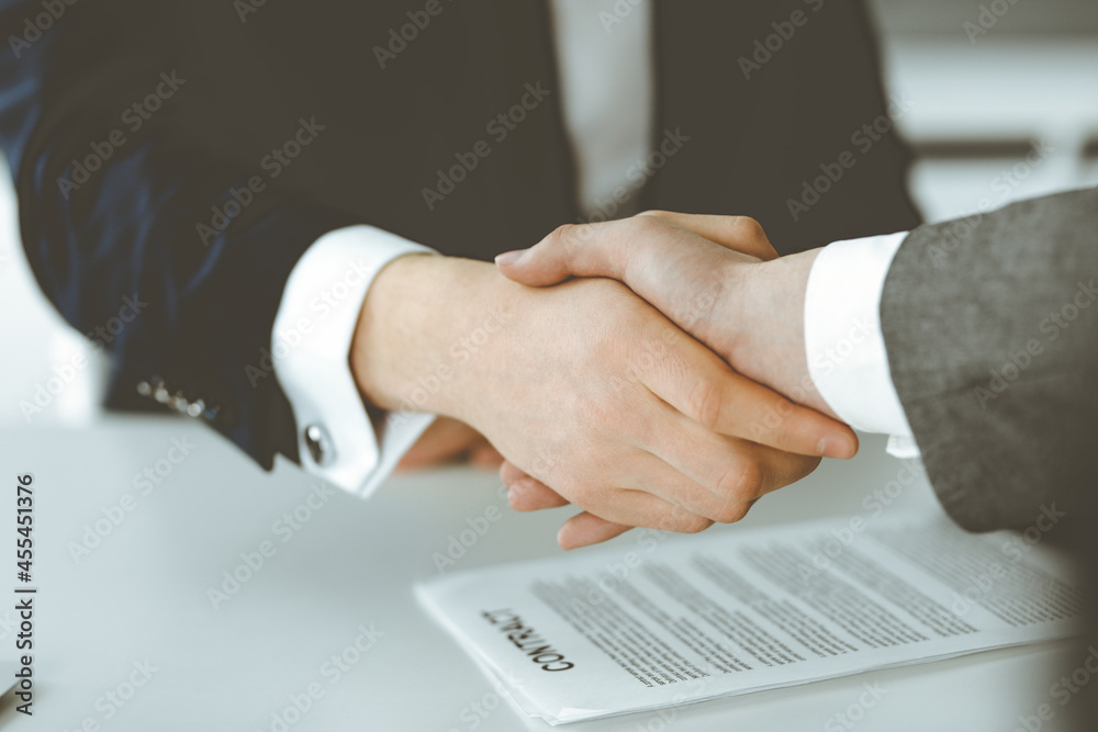 Unknown businessman shaking hands with his colleague or partner above the glass desk in modern office, close-up. Business people group at meeting Unknown businessman shaking hands with his colleague or partner above the glass desk in modern office, close-up. Business people group at meeting