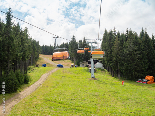 Bild auf Leinwand Chairlift with orange wind cover of seats shaking on the up way through forest
