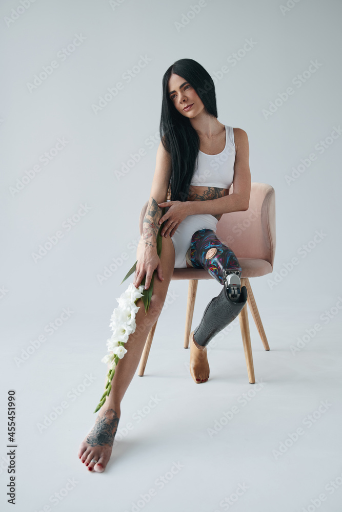 Woman with artificial leg sitting at the chair while posing at the studio with flowers Woman with artificial leg sitting at the chair while posing at the studio with flowers