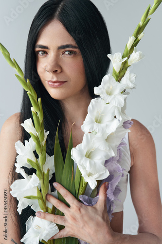 So beautiful. Portrait view of the tender brunette woman posing to the camera with bouquet of gladioli flowers. Female appearance concept photo