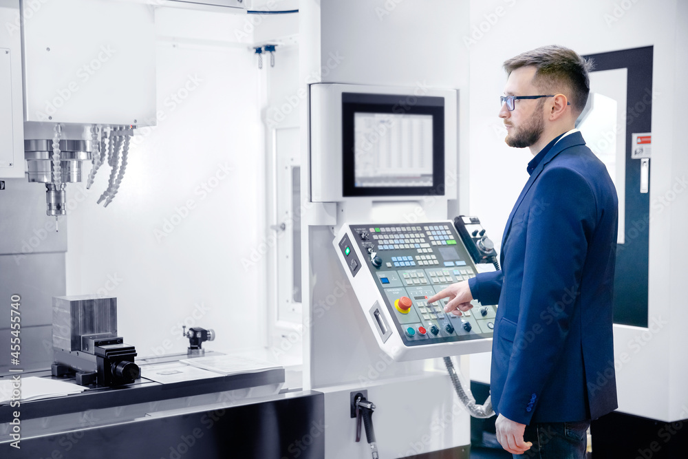 Worker man entering data in CNC machine at automatic factory floor. Modern process metal detail production going for car Worker man entering data in CNC machine at automatic factory floor. Modern process metal detail production going for car