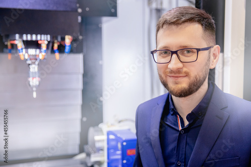 Portrait worker young man in glasses entering data in CNC drill machine at automatic factory floor