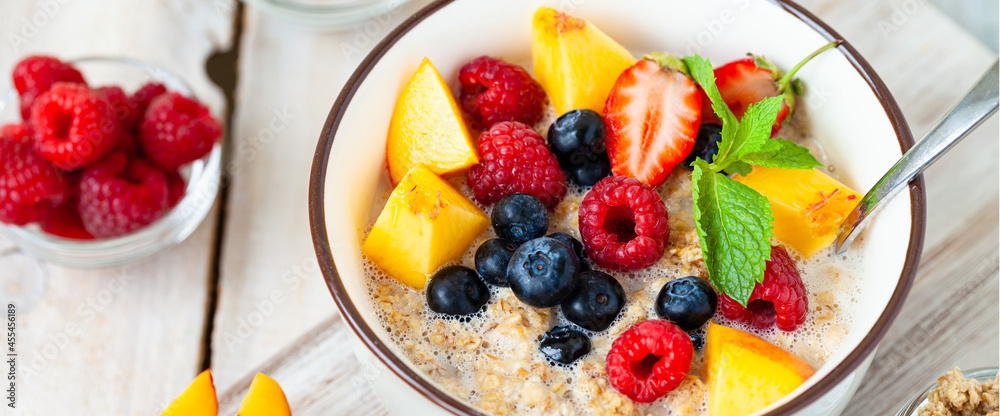 Bowl with vegan granola with fresh ripe organic berries, peach, plant milk, mint. Concept of dieting, detox, tasty simple super food, healthy low calories breakfast. Wooden background, close up banner Bowl with vegan granola with fresh ripe organic berries, peach, plant milk, mint. Concept of dieting, detox, tasty simple super food, healthy low calories breakfast. Wooden background, close up banner