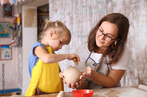 Mother and kid daughter molded from clay at pottery class
