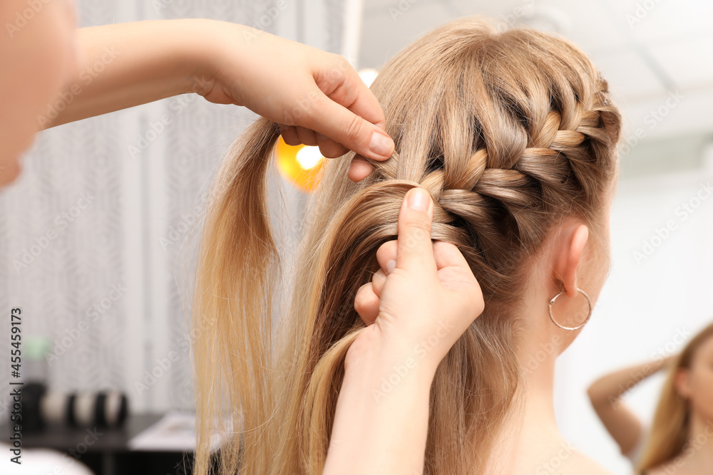 Professional stylist braiding client's hair in salon - obrazy, fototapety, plakaty 