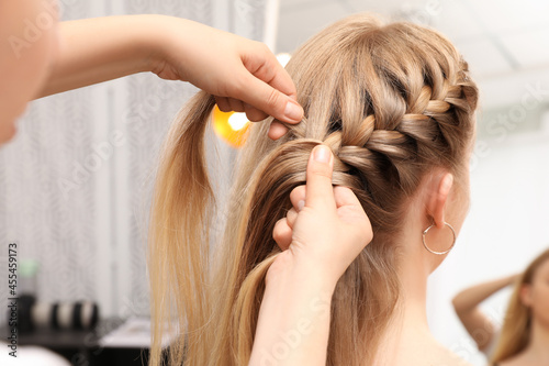 Professional stylist braiding client's hair in salon photo
