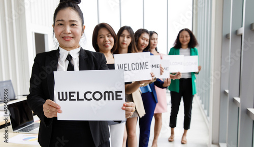 Group of Asian female businesspeople joins together greeting and hold welcome words for a sign of happiness and pleasure for coming of something or someone © Bangkok Click Studio