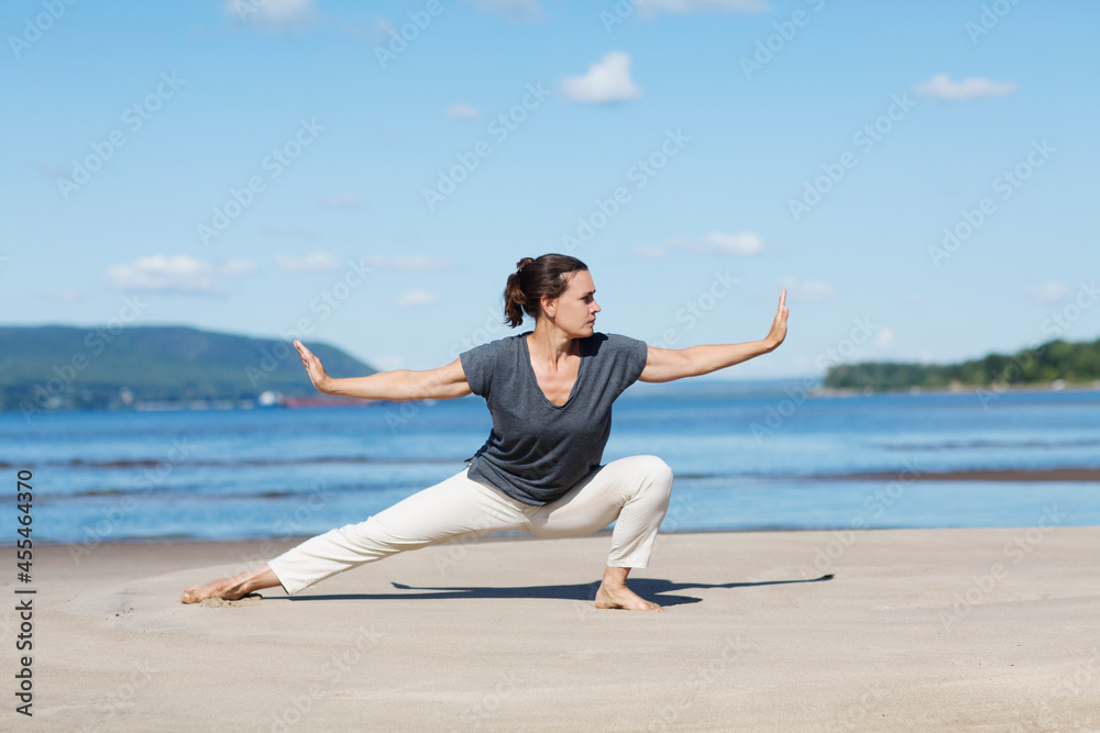 Fototapeta premium Woman praticing tai chi chuan on the beach. Chinese management skill Qi's energy. solo outdoor activities. Social Distancing 