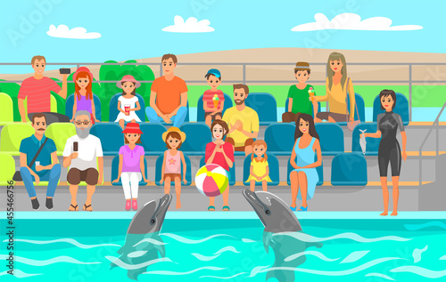 Couple of dolphins is performing in dolphinarium. Dolphins play with ball, do tricks for spectators. Show on water, performance in oceanarium. Viewers watch marine mammals playing with ball in pool