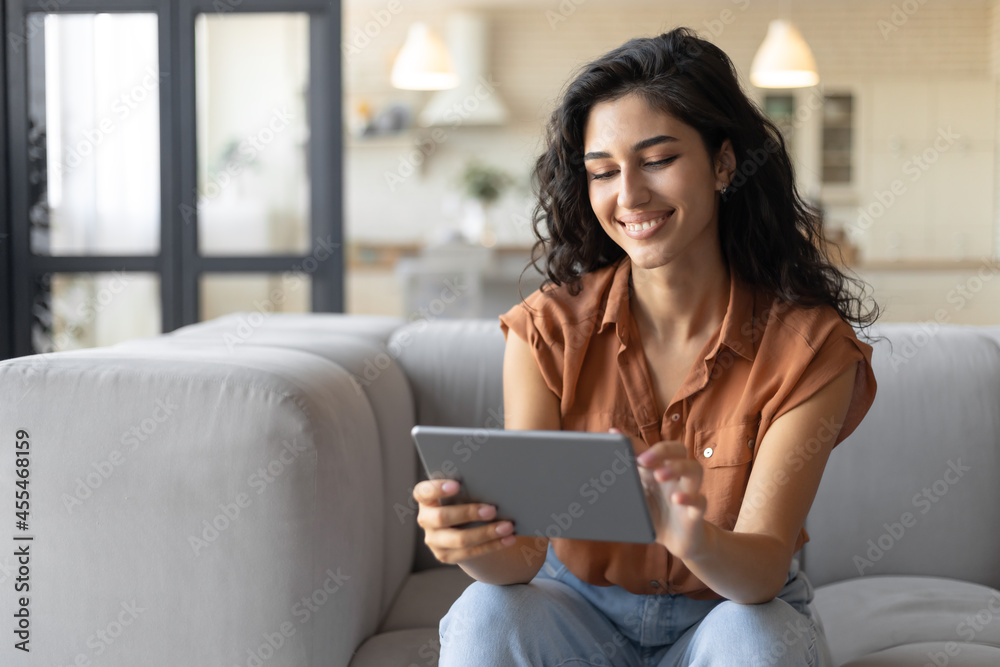 Portrait of smiling young woman using tablet, sitting on couch at home, copy space Portrait of smiling young woman using tablet, sitting on couch at home, copy space
