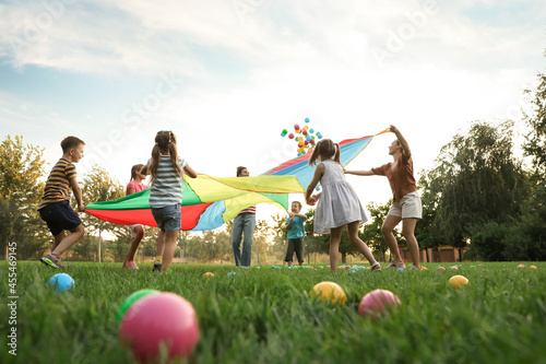 Group of children and teachers playing with rainbow playground parachute on green grass, low angle view. Summer camp activity photo