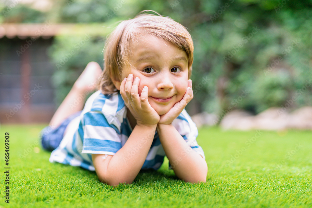Positive toddler boy is lying on the grass in summer. Smiling child spending vacation outdoors. Positive toddler boy is lying on the grass in summer. Smiling child spending vacation outdoors.