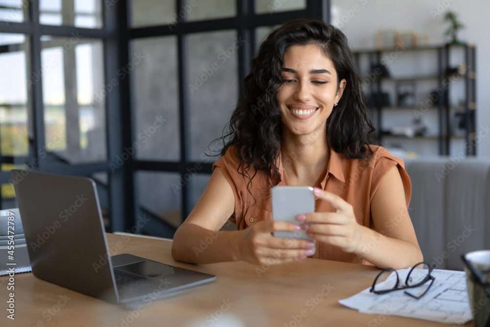 Happy young Caucasian lady using smartphone and laptop for online work at home, copy space Happy young Caucasian lady using smartphone and laptop for online work at home, copy space