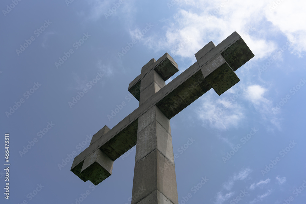 Concrete christian cross on a background of blue sky and white clouds on a sunny day