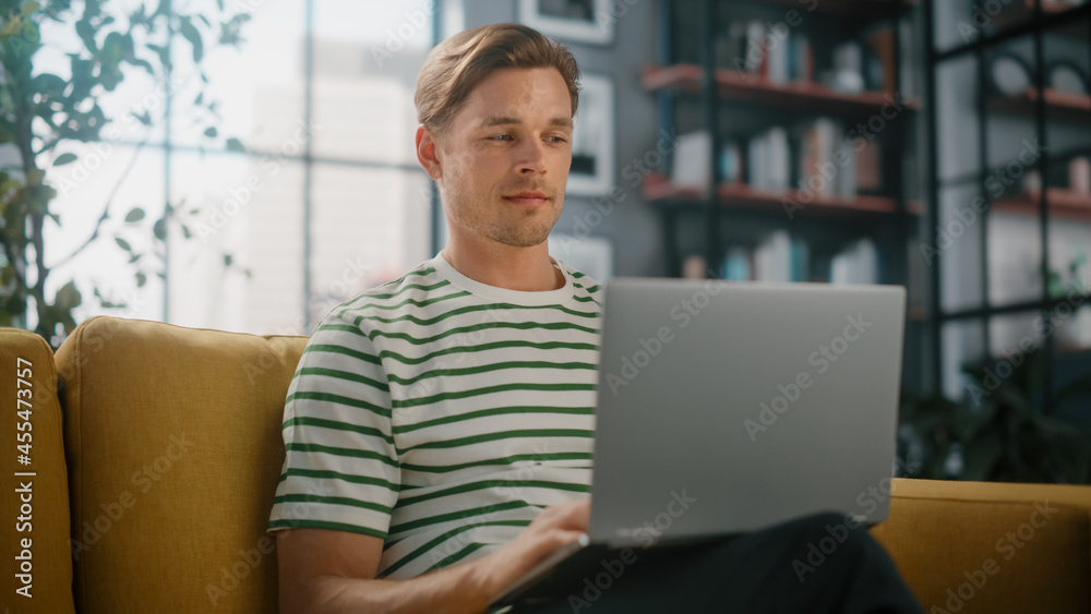 Portrait of a Man Using Laptop at Home Office, Does Remote Work. Handsome Male Sitting on Sofa Works On Computer, Brainstorms Project, does Online Shopping, Browsing Internet, Day Job. Portrait of a Man Using Laptop at Home Office, Does Remote Work. Handsome Male Sitting on Sofa Works On Computer, Brainstorms Project, does Online Shopping, Browsing Internet, Day Job.