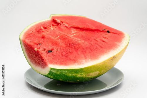 Half of a red watermelon lies in a plate on a uniform background. Healthy vegetarian food