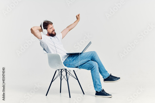 man in white t-shirt sitting on a chair with a laptop in headphones entertainment