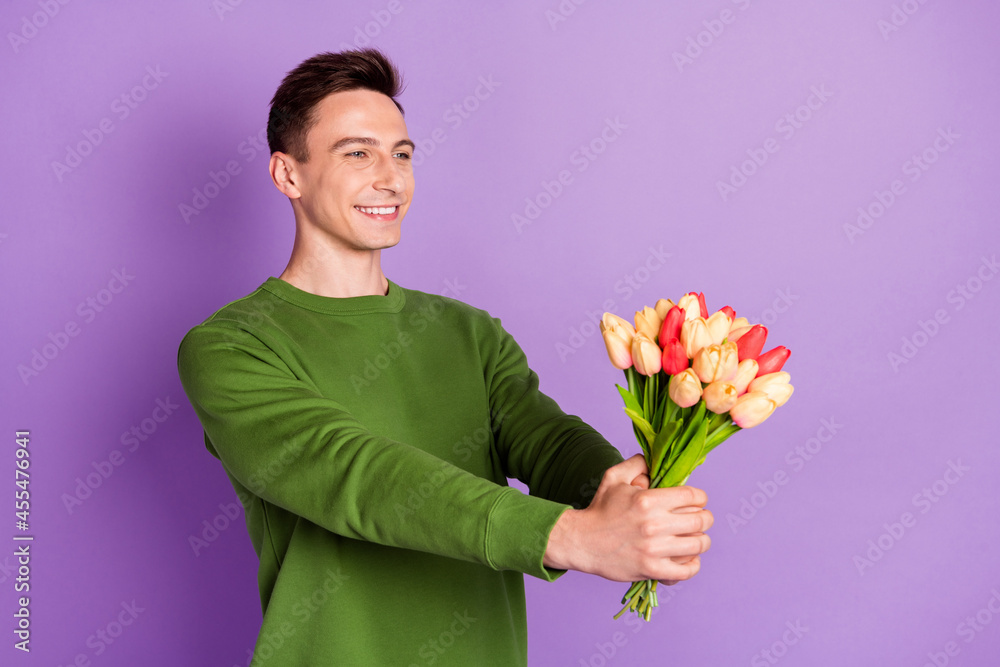 Photo of millennial cute brunet guy give flowers wear sweater isolated on purple background Photo of millennial cute brunet guy give flowers wear sweater isolated on purple background