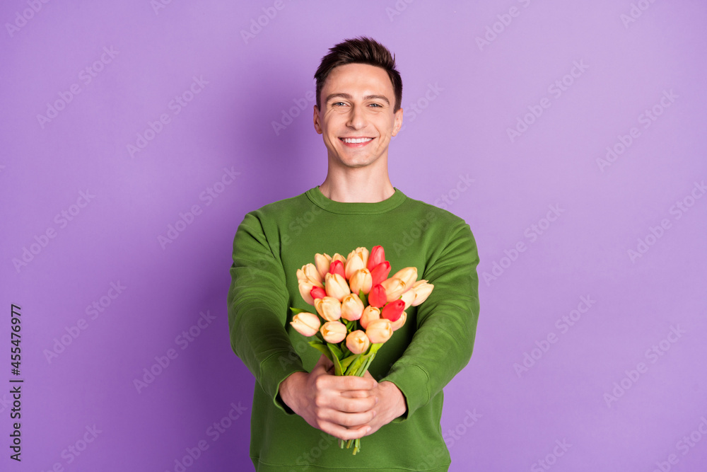 Photo of young flirty brunet guy give flowers wear sweater isolated on purple background Photo of young flirty brunet guy give flowers wear sweater isolated on purple background