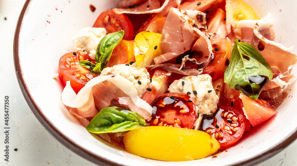 Diet menu. Healthy salad of fresh vegetables with tomatoes, cream cheese balls, prosciutto jamon and basil leaves on a bowl. Flat lay. Banner. Top view