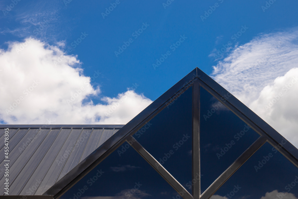Part of the triangular roof of a modern wooden house against the bright sky in the background.