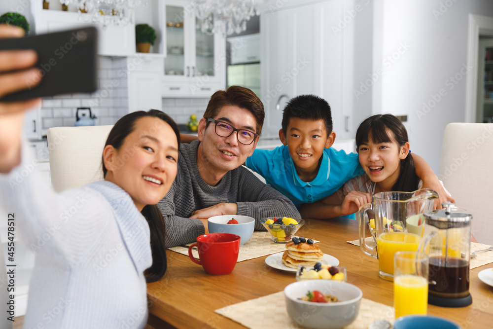 Smiling asian parents with son and daughter sitting at breakfast table taking selfie Smiling asian parents with son and daughter sitting at breakfast table taking selfie