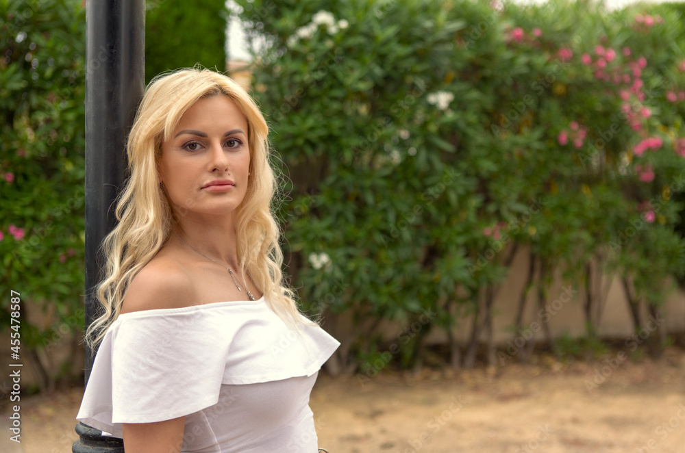 beautiful long-haired blonde woman in her 40s leaning against a lamppost in a park beautiful long-haired blonde woman in her 40s leaning against a lamppost in a park