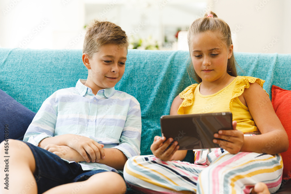 Happy caucasian brother and sister sitting on couch and using tablet in living room Happy caucasian brother and sister sitting on couch and using tablet in living room