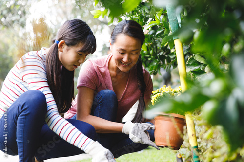 Happy asian mother and daughter smiling, wearing gloves and working in garden