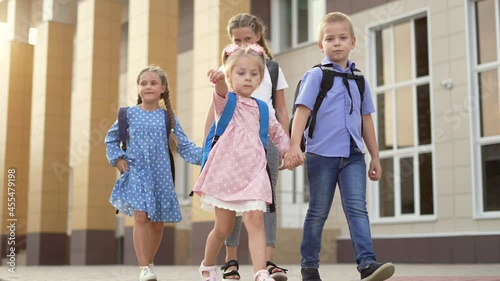 Children return to school with backpacks. Family of children goes to school. Happy family concept. Children go to school holding hands. Study offline. Children with books and backpacks go to school