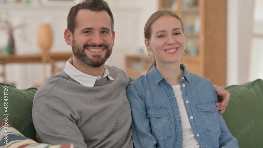 Happy Couple Smiling at the Camera while Sitting on Sofa Happy Couple Smiling at the Camera while Sitting on Sofa