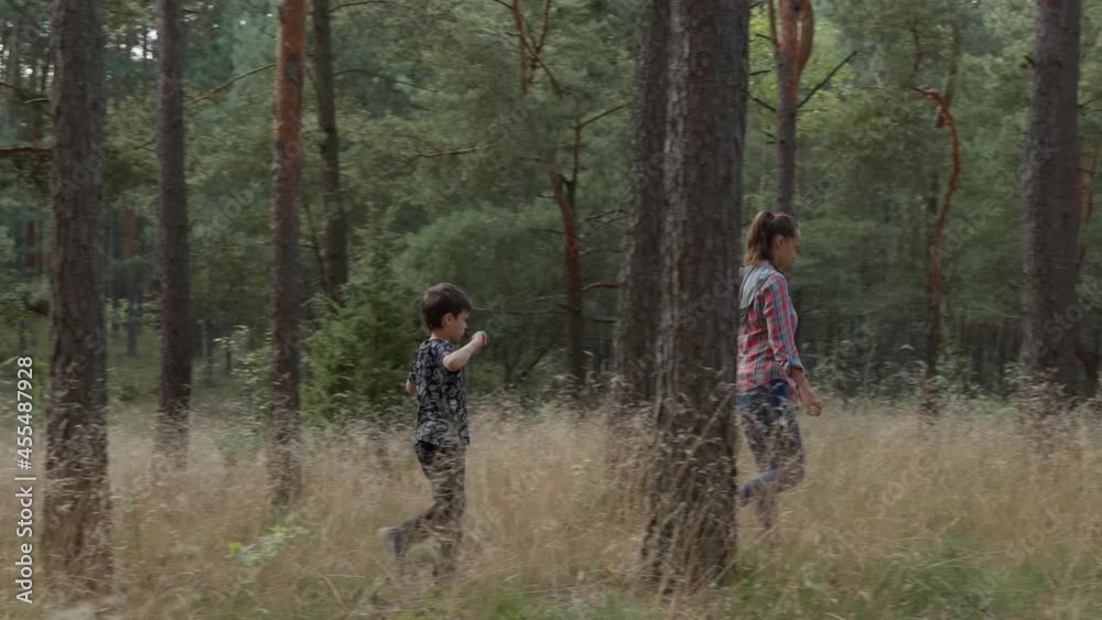 A woman and a boy are walking in the forest between the trees A woman and a boy are walking in the forest between the trees