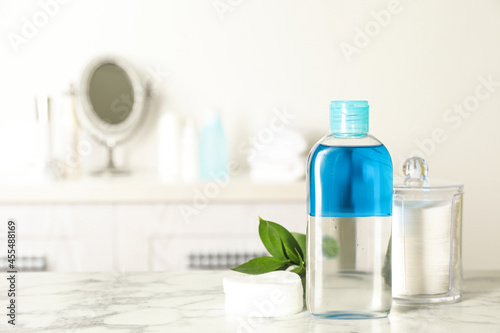 Cotton pads, leaves and makeup removal product on white marble table in bathroom. Space for text photo