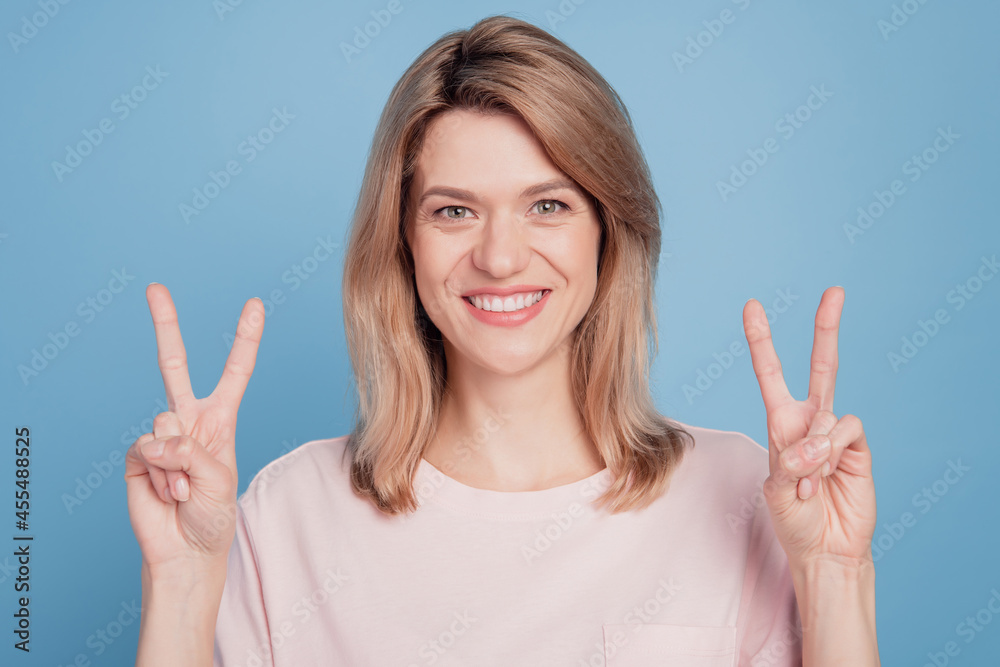 Portrait of cheerful cute girl fingers show victory sign beaming smile on blue background