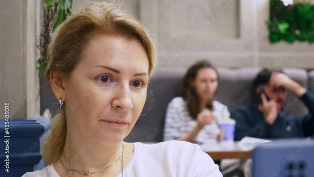 A woman in a restaurant is surprised by the news from the network, looks through the news from the Internet with wide eyes. Unrecognizable people are out of focus in the background. A woman in a restaurant is surprised by the news from the network, looks through the news from the Internet with wide eyes. Unrecognizable people are out of focus in the background.