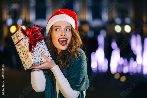 smiling girl in a green shawl, holding a gift box, on the background of the evening city. new year gift, winter shopping